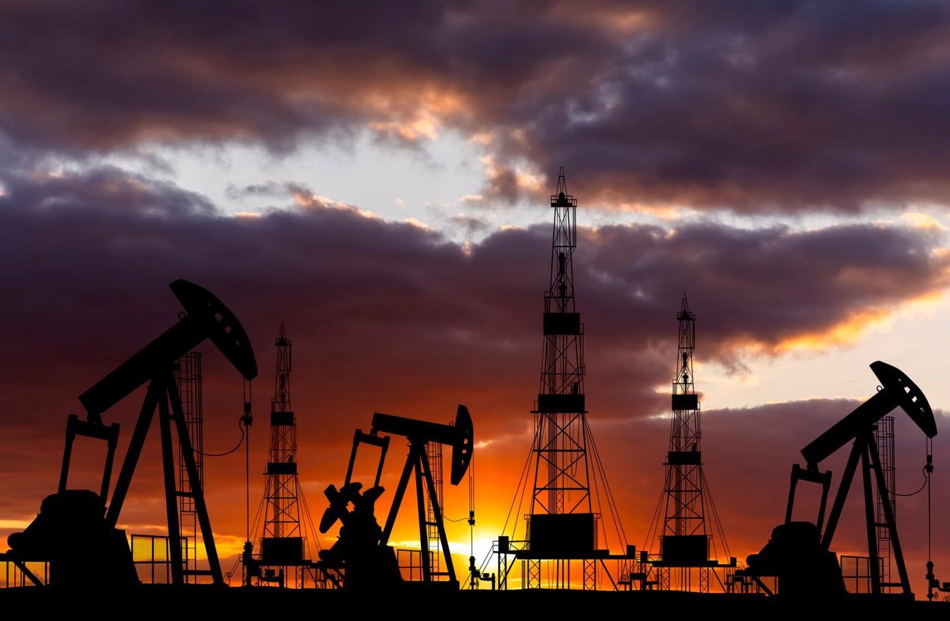 Oil rigs silhouetted against a vibrant sunset sky in Africa.