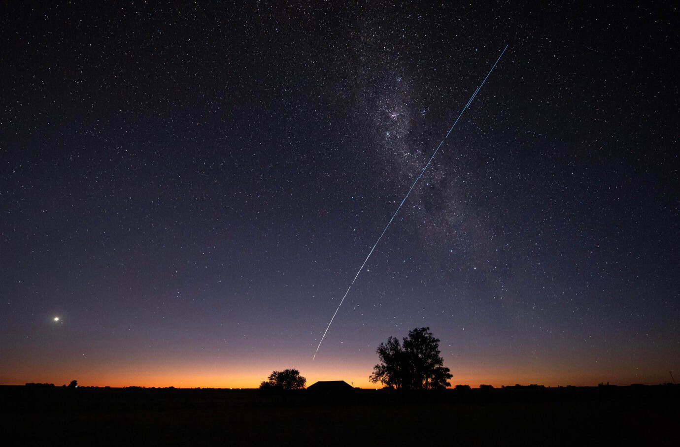 Bright stars and a shooting star streak across the night sky, showcasing celestial beauty.
