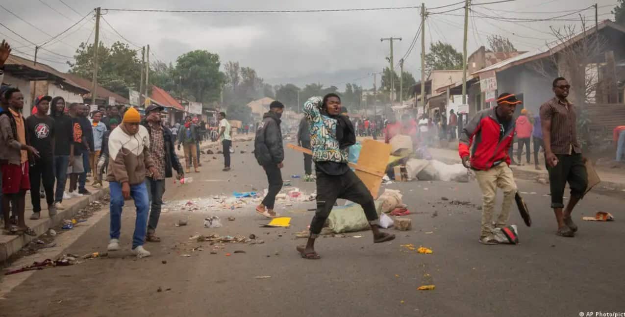 People walking through a chaotic street with debris, smoke, and damaged surroundings.