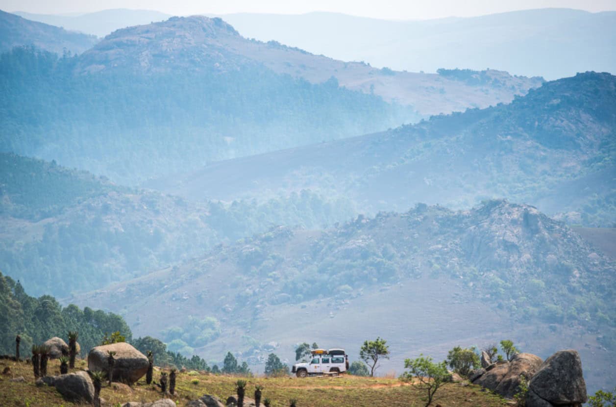 Scenic African mountain landscape with grazing animals and a vehicle in the foreground.