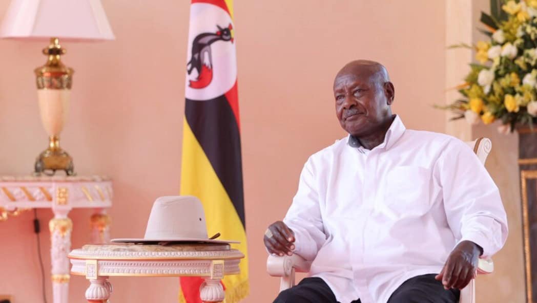Kenyan official seated during formal meeting with Uganda flag in background.