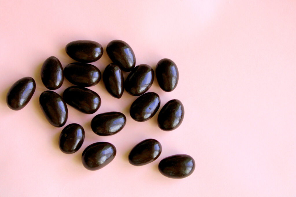 Black jelly beans on a pink background.