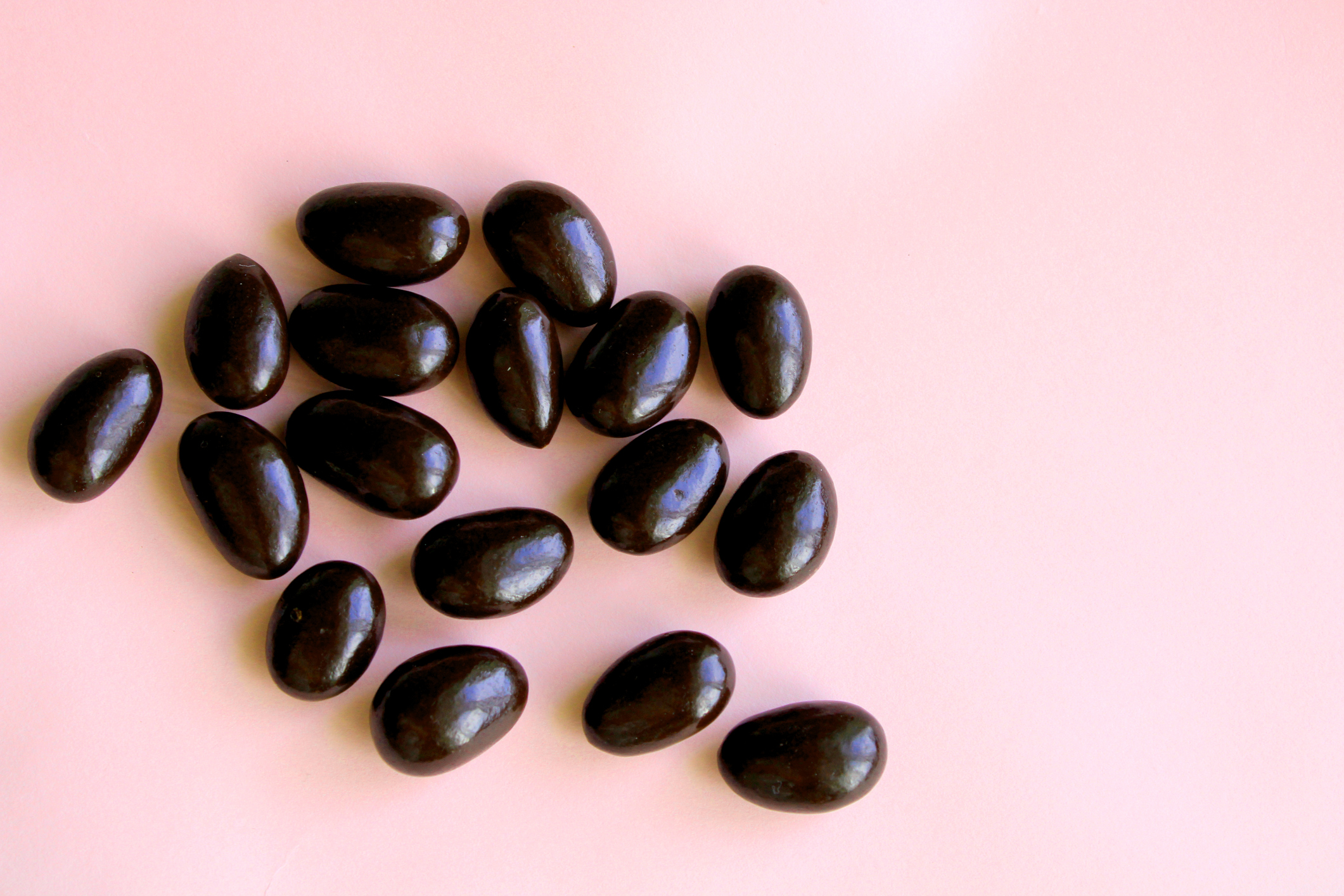 Black jelly beans on a pink background.