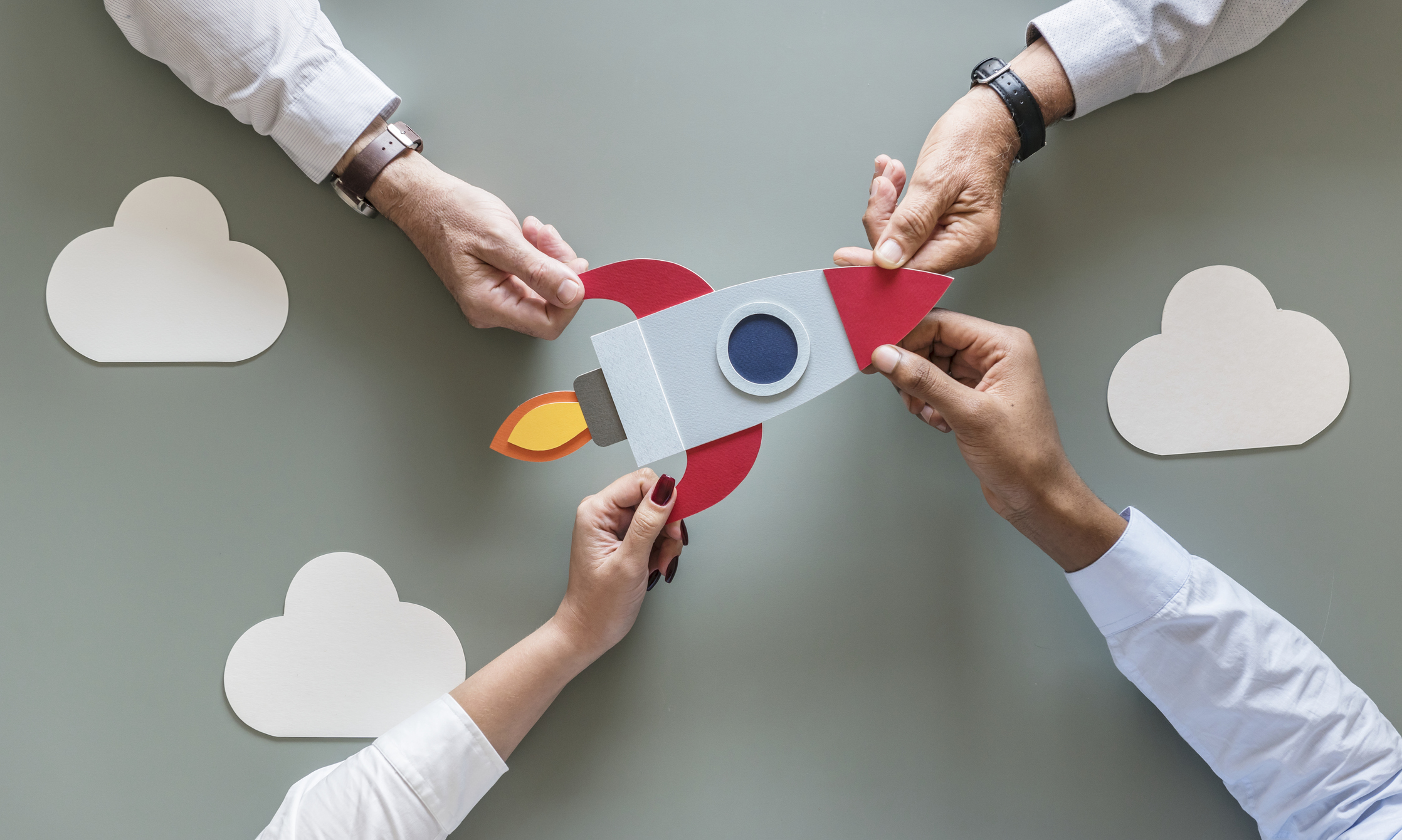 Three pairs of hands assembling a paper rocket ship, symbolizing collaboration and the excitement of launching a new business.