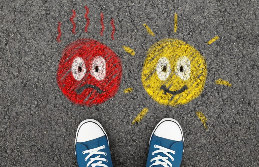 A pair of blue sneakers standing between two chalk-drawn faces on asphalt — one red and agitated, one yellow and cheerful — illustrating the choice between a difficult client and a good one.
