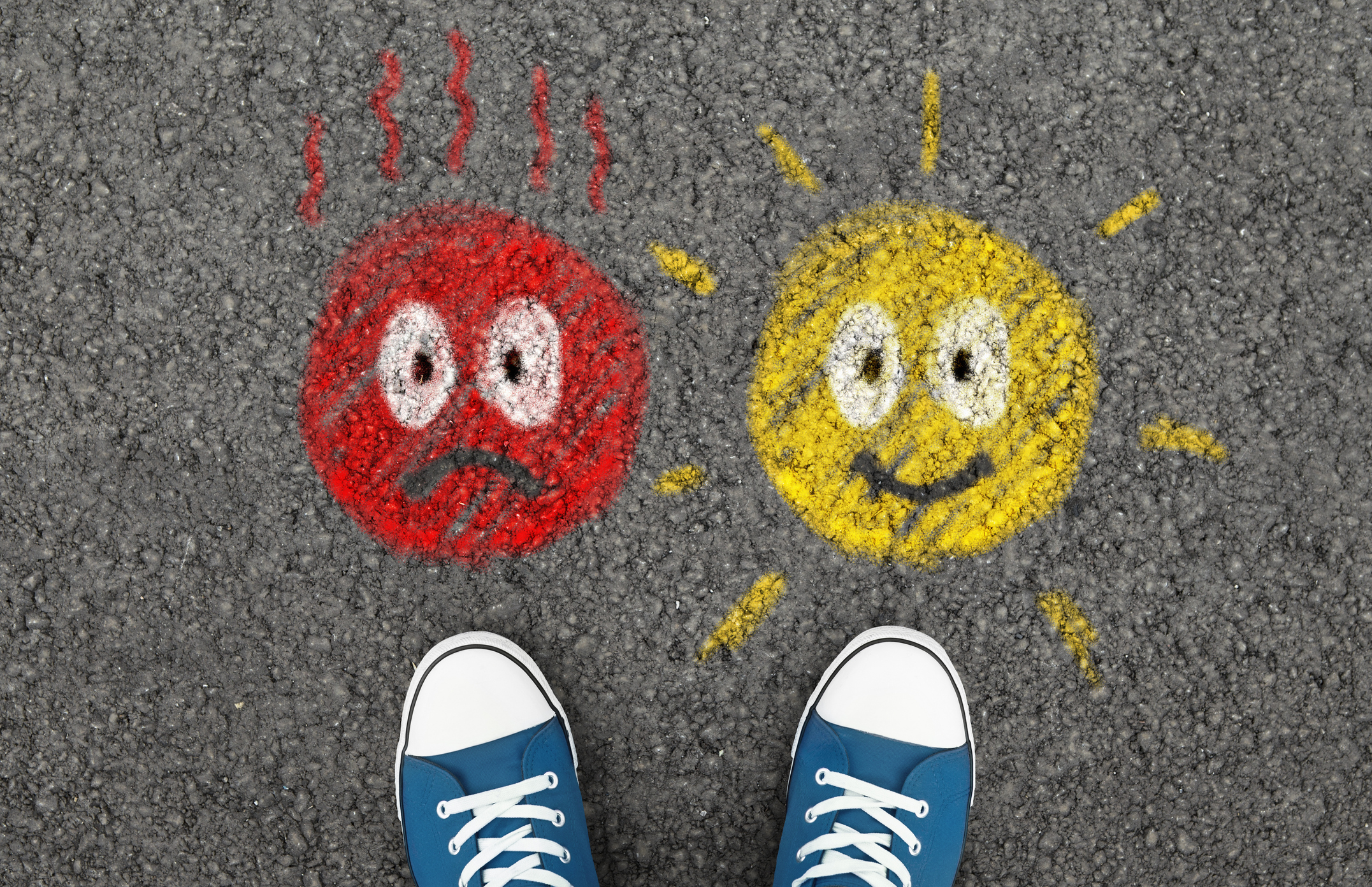 A pair of blue sneakers standing between two chalk-drawn faces on asphalt — one red and agitated, one yellow and cheerful — illustrating the choice between a difficult client and a good one.