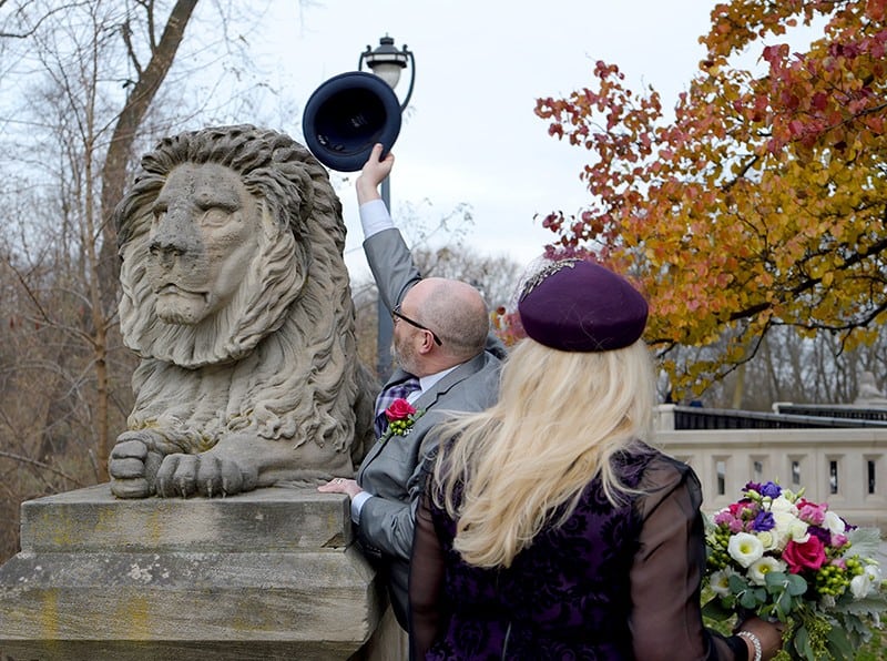 Wedding day photo of John Carr putting hat on lion sculpture, Rochelle looking on.