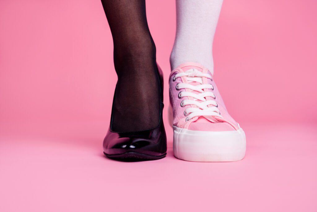 Two mismatched shoes side by side against a pink background — one a sleek black stiletto, one a pink canvas sneaker — illustrating the idea that your brand identity sets the tone for everything that follows.