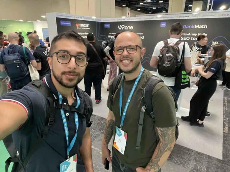 Due partecipanti alla conferenza posano per un selfie allo stand di GroupOne, con la segnaletica degli strumenti SEO e Performance di WordPress in evidenza.