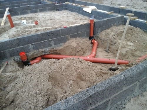 Installation af kloakrør i byggegrund med betonmur og sandbund.