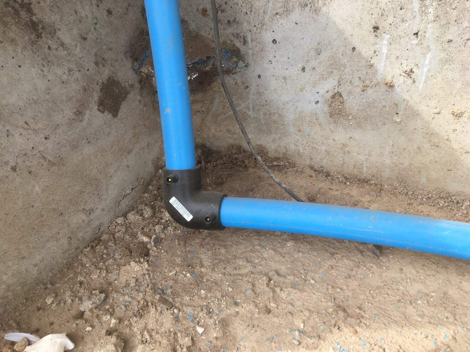 Blå VVS-rør installeret i jorden ved væggen.