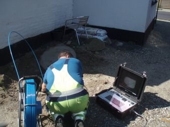 Mand arbejder med kloak- eller jordarbejde udendørs med værktøj og udstyr.