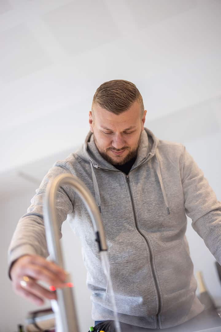 Nærbillede af VVS installatør der fejlfinder på rør under køkkenvasken.