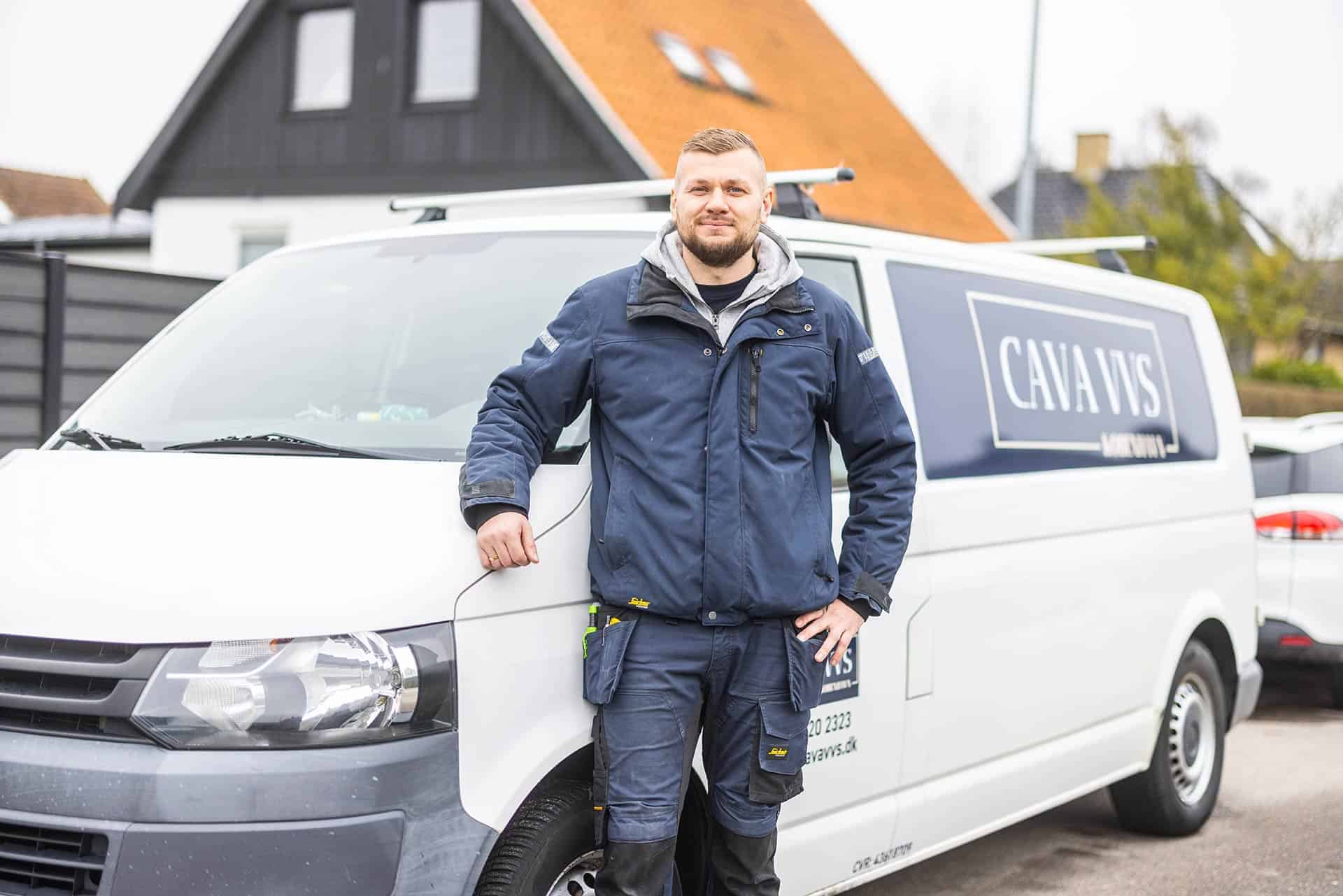 Cava VVS montør i arbejdstøj stående på en villavej ved sin bil.
