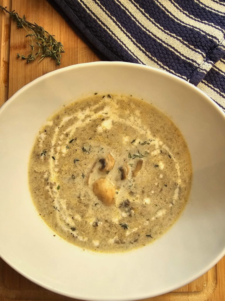 A bowl of creamy and comforting mushroom soup sits on a cutting board
