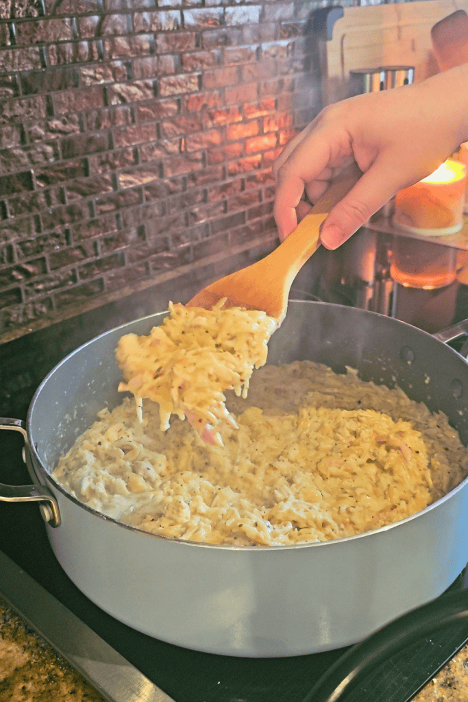 Creamy garlic Parmesan chicken orzo being served in a skillet with a wooden spoon.