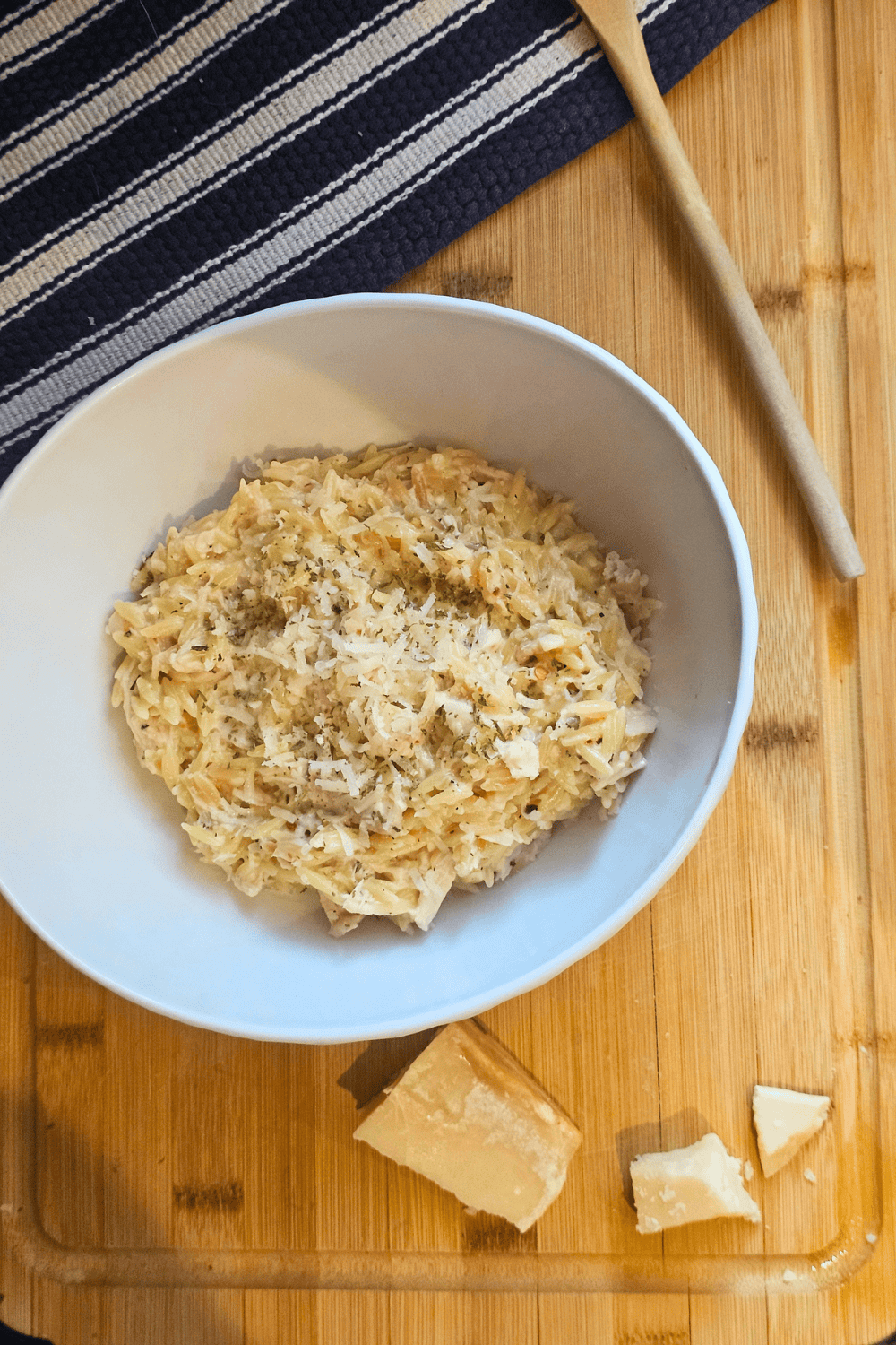 Creamy garlic Parmesan chicken orzo in a white bowl, garnished with cheese, on a wooden table.