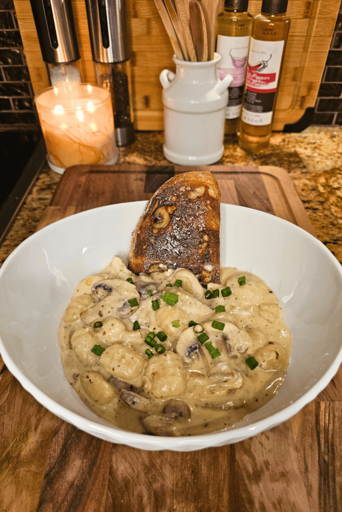 Creamy Boursin gnocchi with mushrooms garnished with chopped green onions in a white bowl.