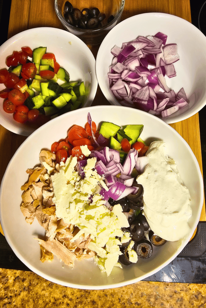 Fresh Greek chicken rice bowl with cucumbers, cherry tomatoes, red onions, olives, and feta cheese.