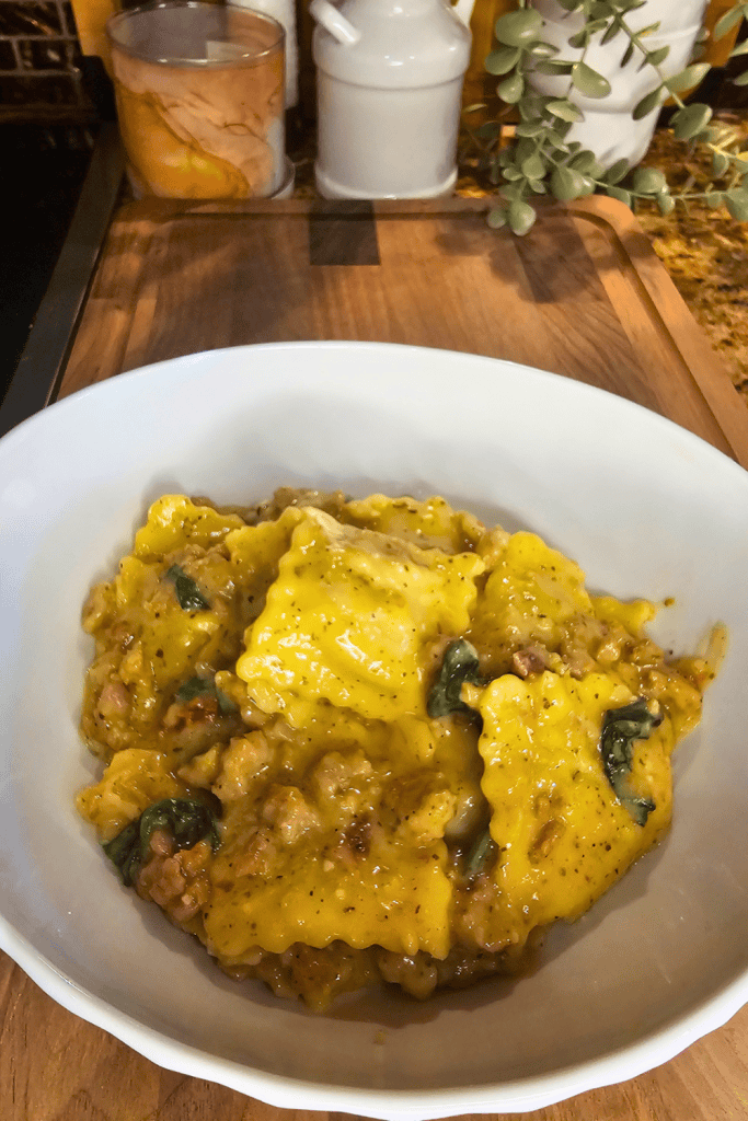Hearty ravioli soup with vegetables and herbs in a white bowl on a wooden table.