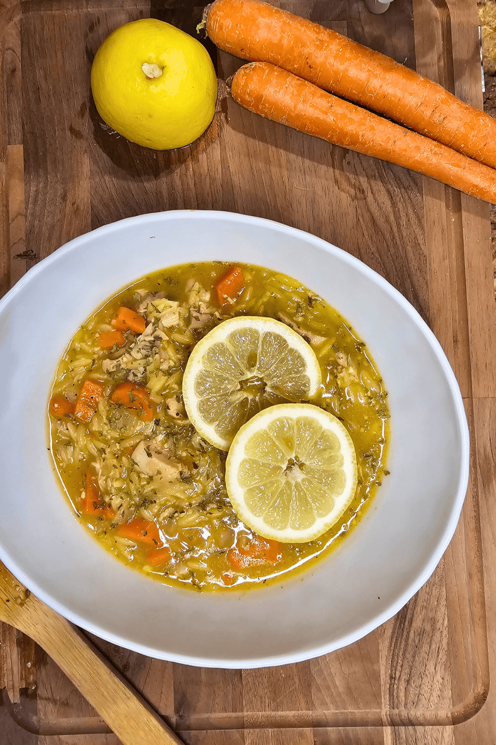 Healthy chicken soup with lemon slices, carrots, and rice in a white bowl.