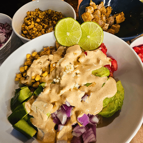 Healthy chicken and veggie bowl with creamy sauce, cucumbers, and lime garnish.