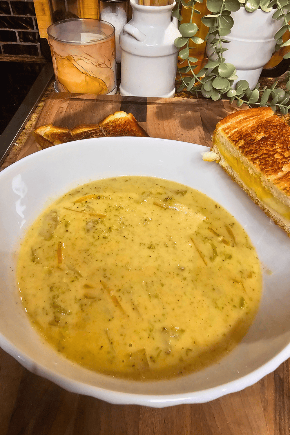 Creamy broccoli cheddar soup served in a white bowl with toast on a wooden table.