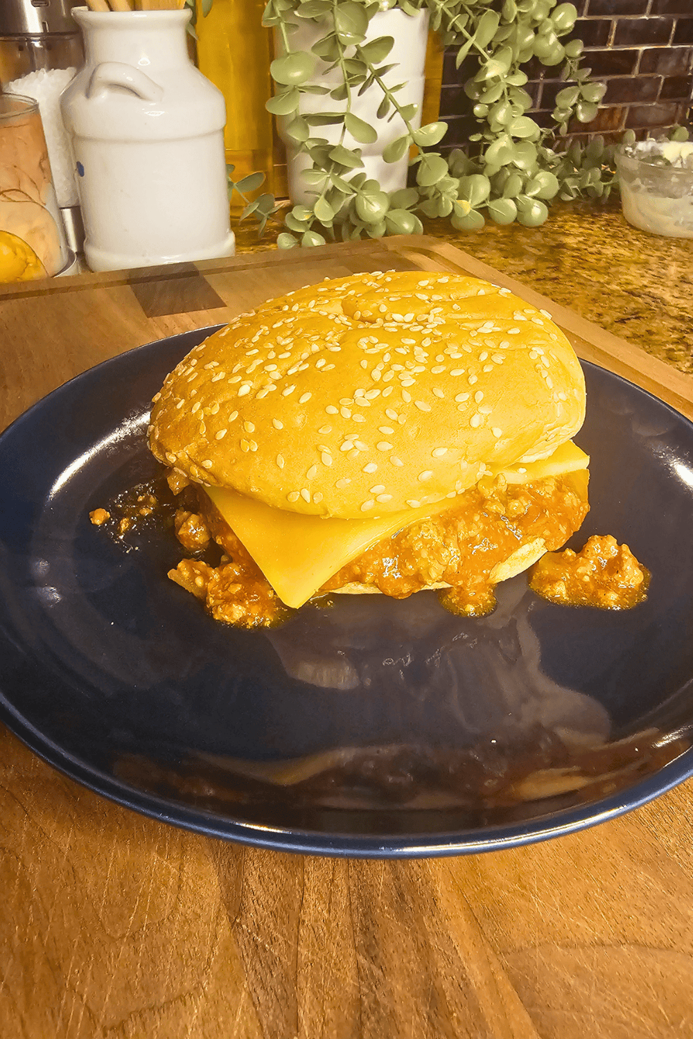 Delicious homemade Sloppy Joes in a sesame seed bun on a black plate.