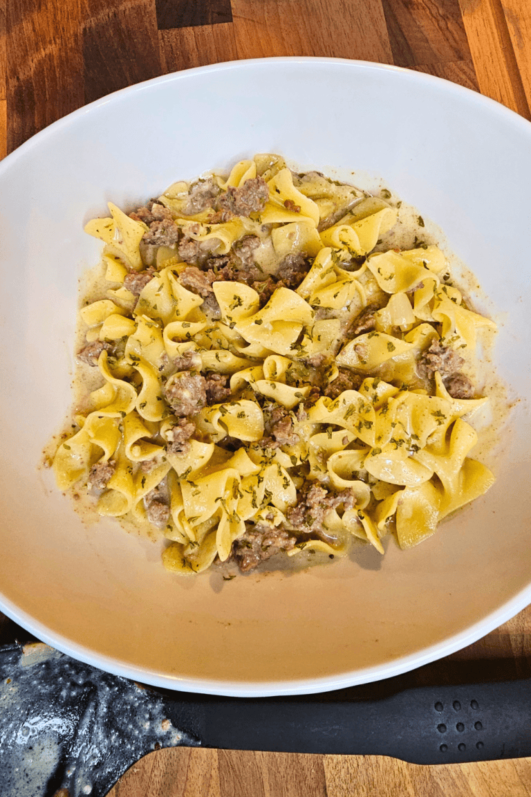 Creamy beef stroganoff with pasta in a white bowl on wooden table.