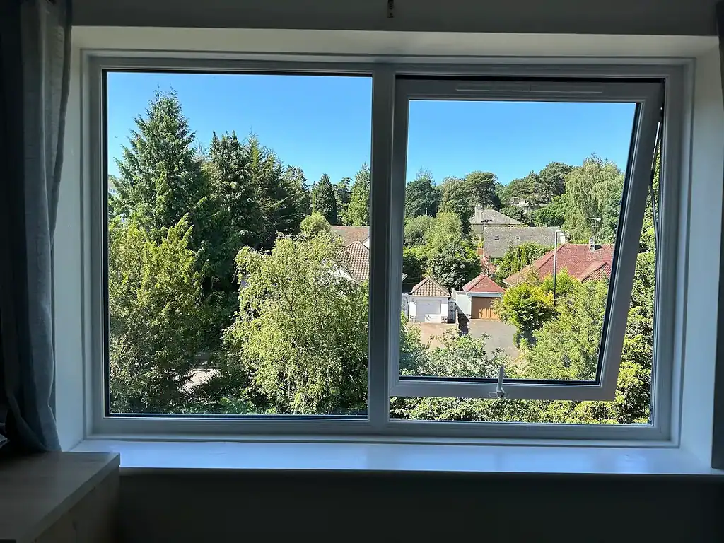 Bright double-glazed uPVC window with a scenic view of trees and houses, installed by CP Glazing Ltd.