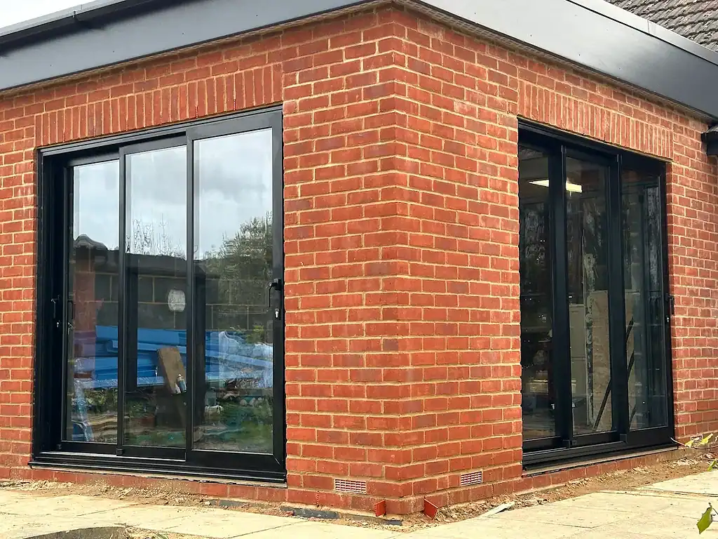 Modern black-framed sliding glass doors installed on a brick building for enhanced safety and insulation.