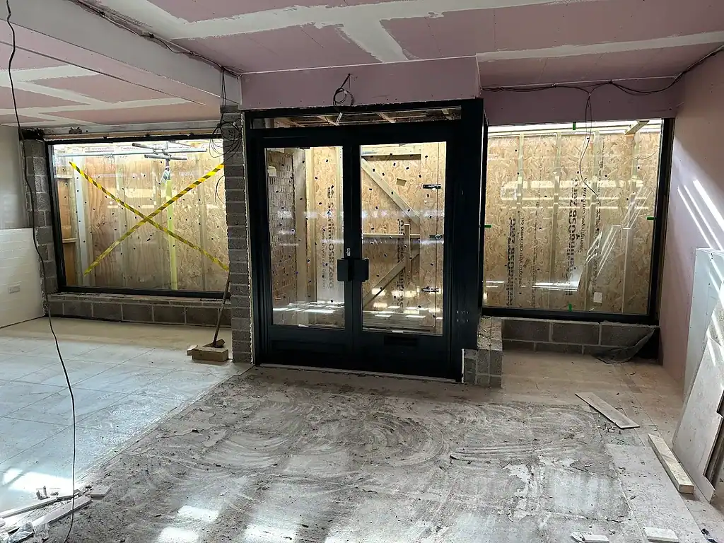 Large black aluminium sliding door installation in progress at a building site with ongoing construction work.
