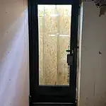 Modern black UPVC door with double glazed glass and protective peeling film, under construction at a building site.
