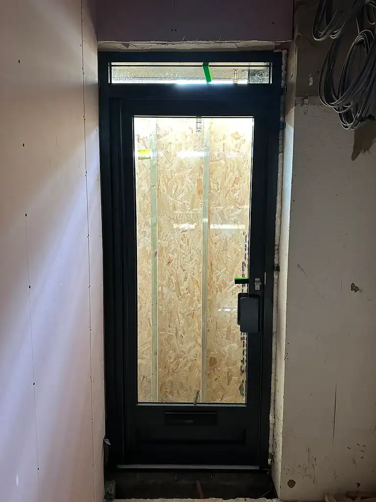 Modern black UPVC door with double glazed glass and protective peeling film, under construction at a building site.