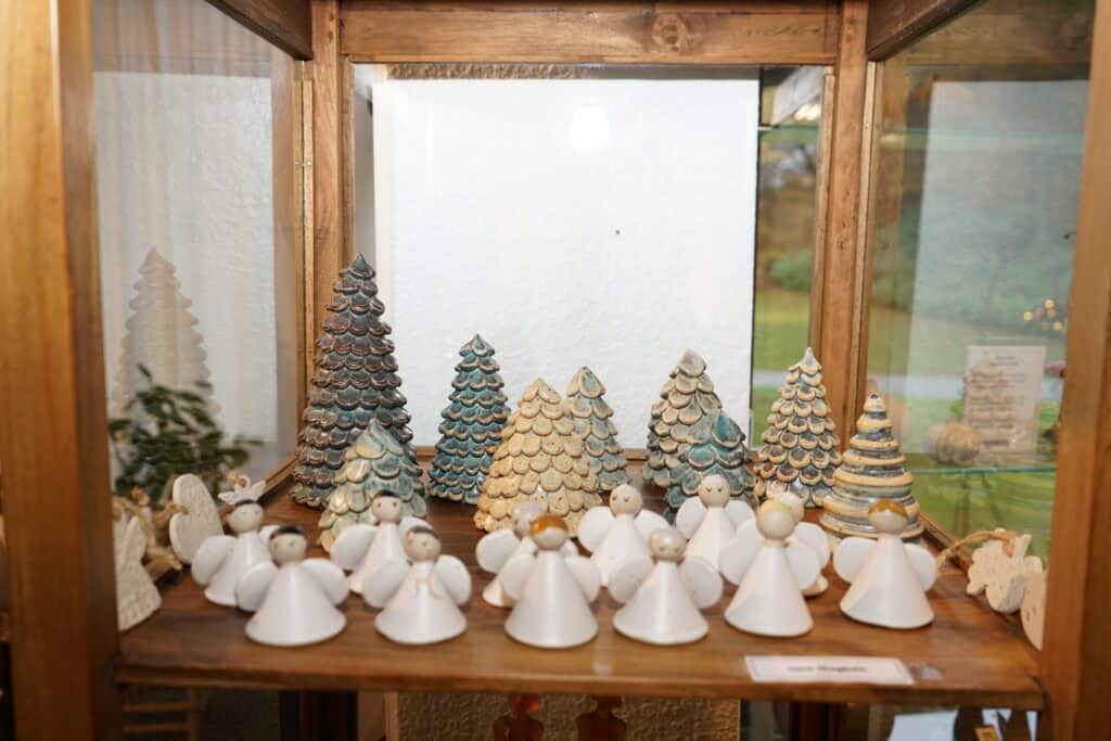 Farverige juletræer og julestadsfigur lavet af keramik i kunsthåndværkstil.