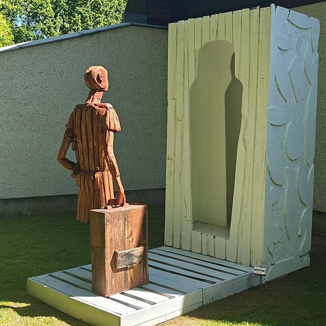 Kunstinstallation med figur foran en stor, kunstnerisk dør ved Dronninglund Kunstcenter.