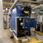 Chaudière industrielle Unilux installée dans une salle mécanique, avec système de drainage indirect et conduites isolées pour la distribution efficace de vapeur.