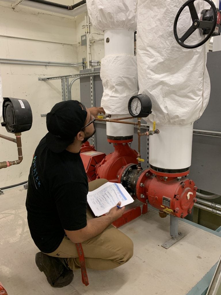 Mécanicien de machines fixes Technicien d’Ecowaterlab en pleine inspection d’un système de tuyauterie industrielle, effectuant une lecture de manomètre pour assurer un fonctionnement optimal.