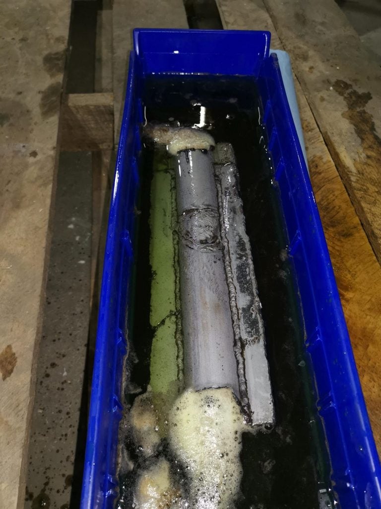 Tuyaux métalliques fortement encrassés plongés dans un bain de nettoyage chimique pour illustrer le processus de désembouage ou de détartrage industriel chez Ecowaterlab.
