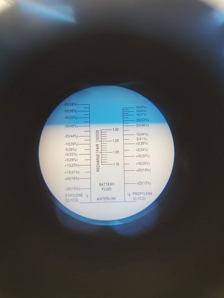 Lecture d’un réfractomètre montrant les niveaux de glycol (éthylène et propylène) et la densité du fluide de batterie, utilisé pour analyser la concentration antigel dans un système de traitement thermique.