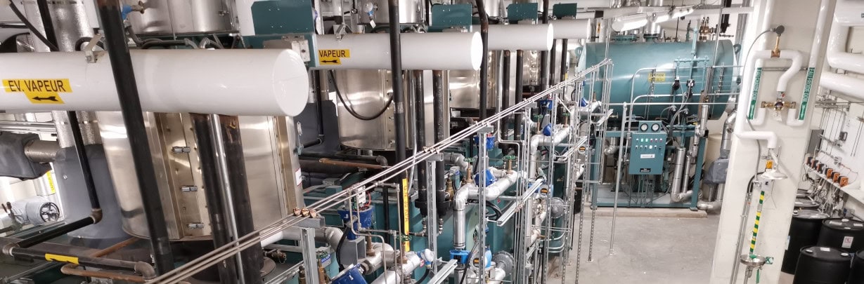Salle technique industrielle équipée de systèmes de traitement d’eau Ecowaterlab avec tuyauterie, réservoirs pressurisés et vannes automatisées.