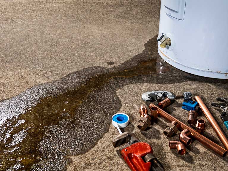 A pool of water leaks out from the base of a white water heater unit.
