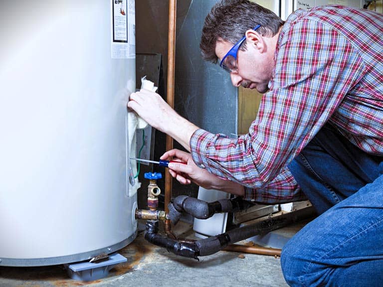 A water heater technician works on fixing a large white water heater unit.