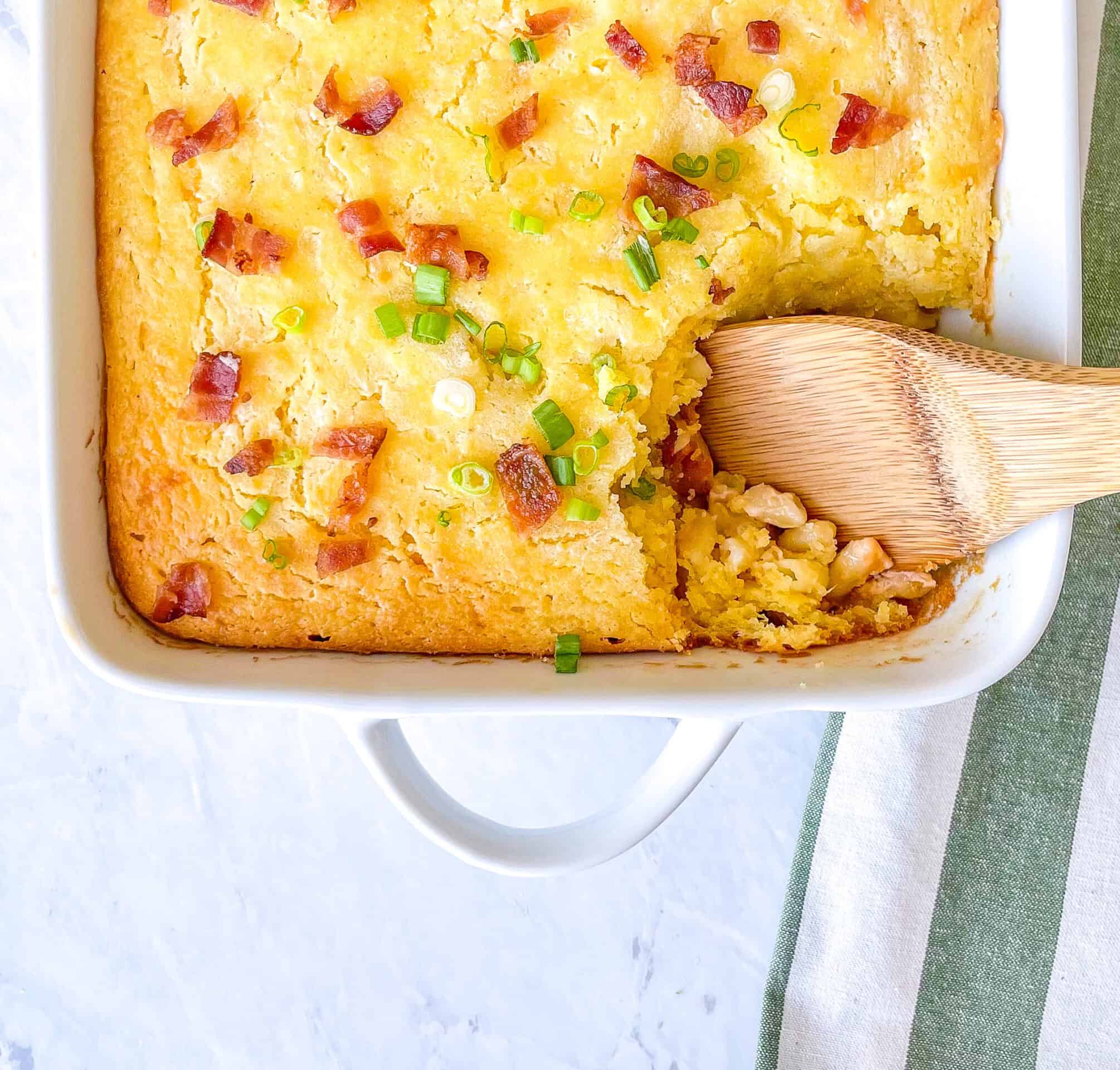 Casserole dish containing cornbread casserole with bacon and green onions on top