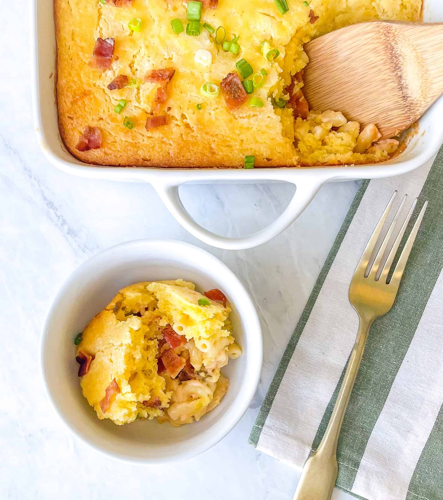 bowl containing cornbread casserole next to the casserole serving dish and green and white striped towel..