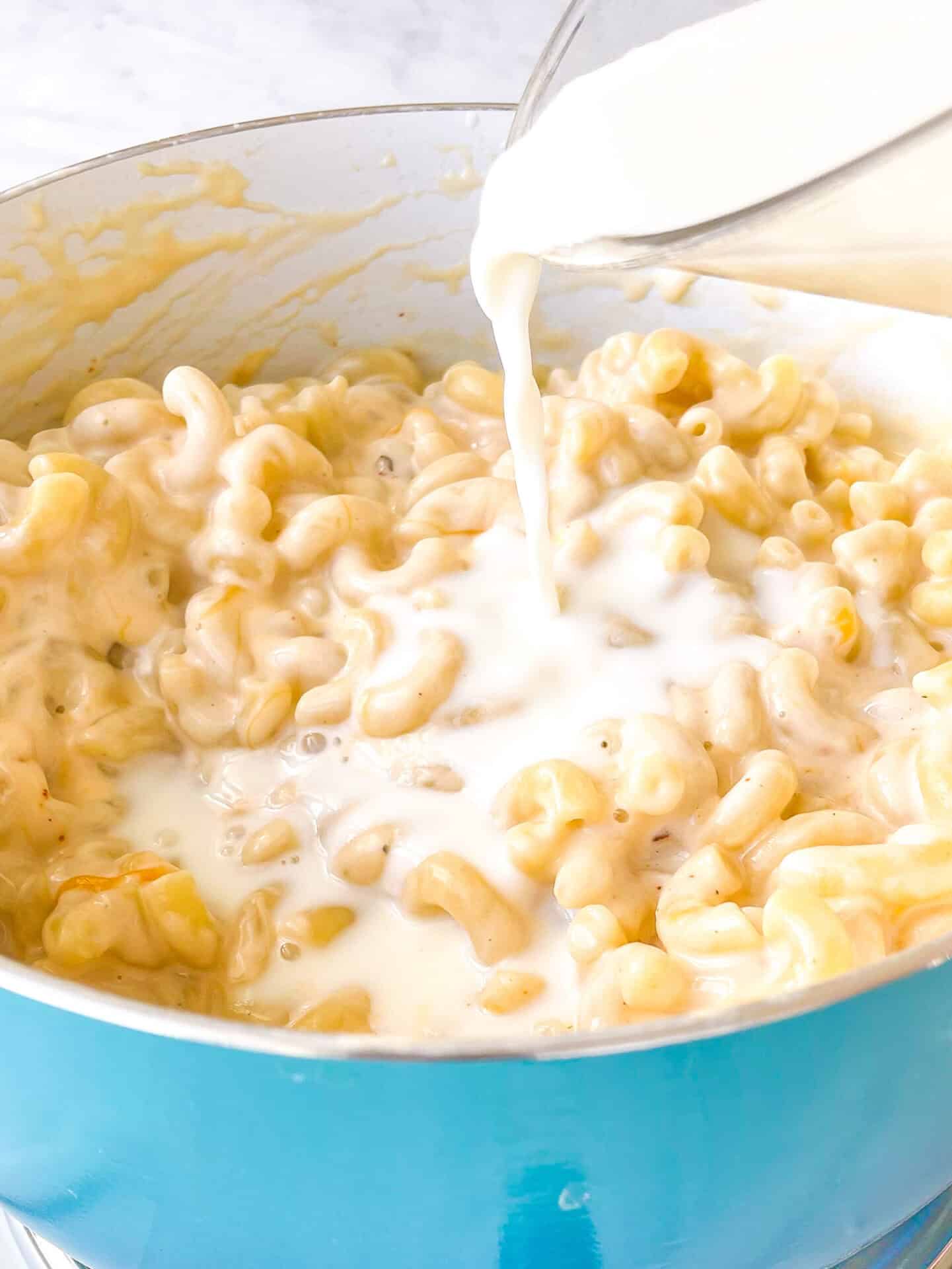 Blue pot with milk pouring into macaroni and cheese mixture