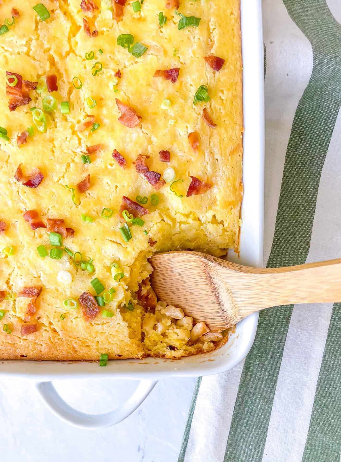 Casserole dish containing cornbread casserole with bacon and green onions on top