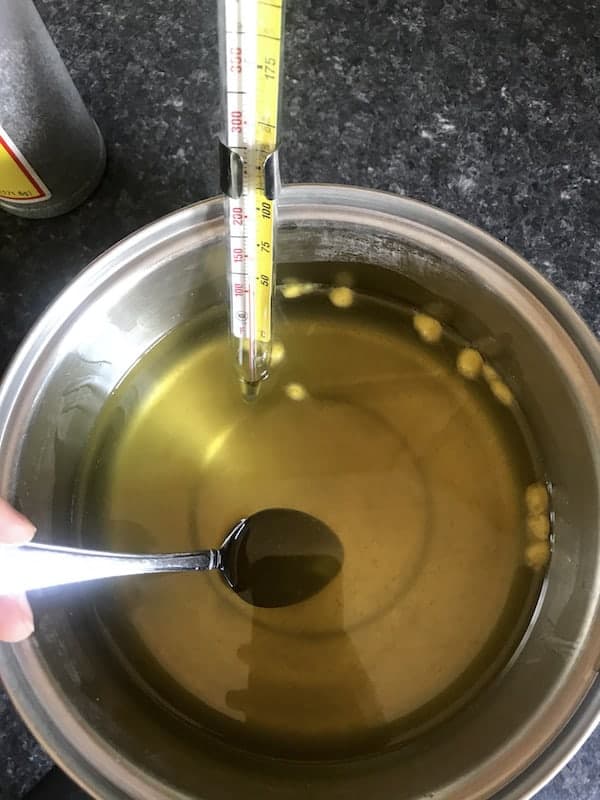 Image shows a pot full of melted oils for soap, with a thermometer
