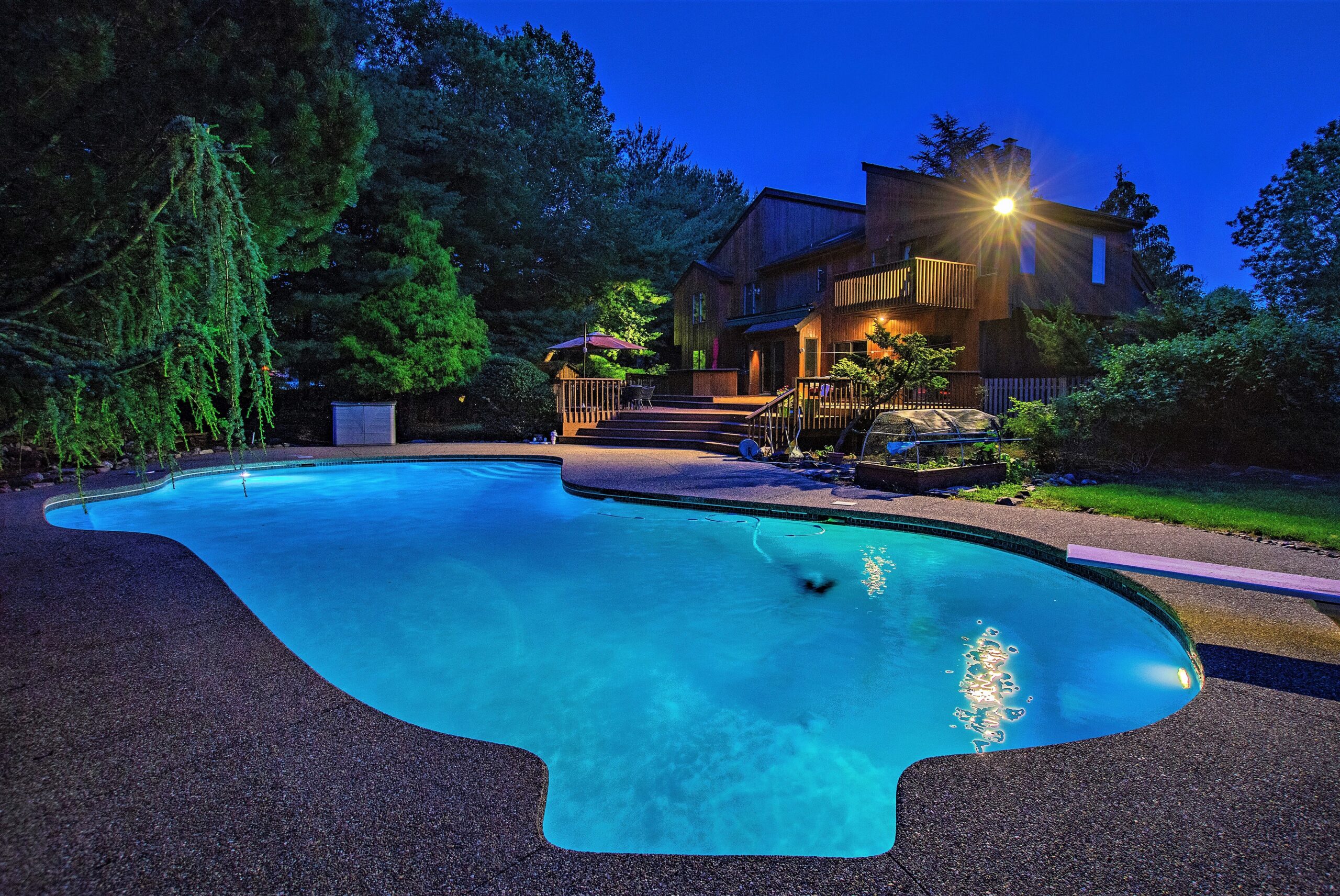 Twilight pool scene with illuminated water framed by home and deck.