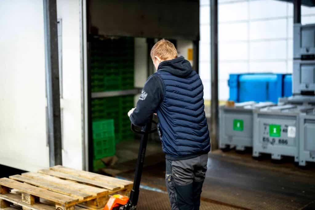 Vognmand håndterer træpaller og udstyr bag ved en lastbil på en plads.